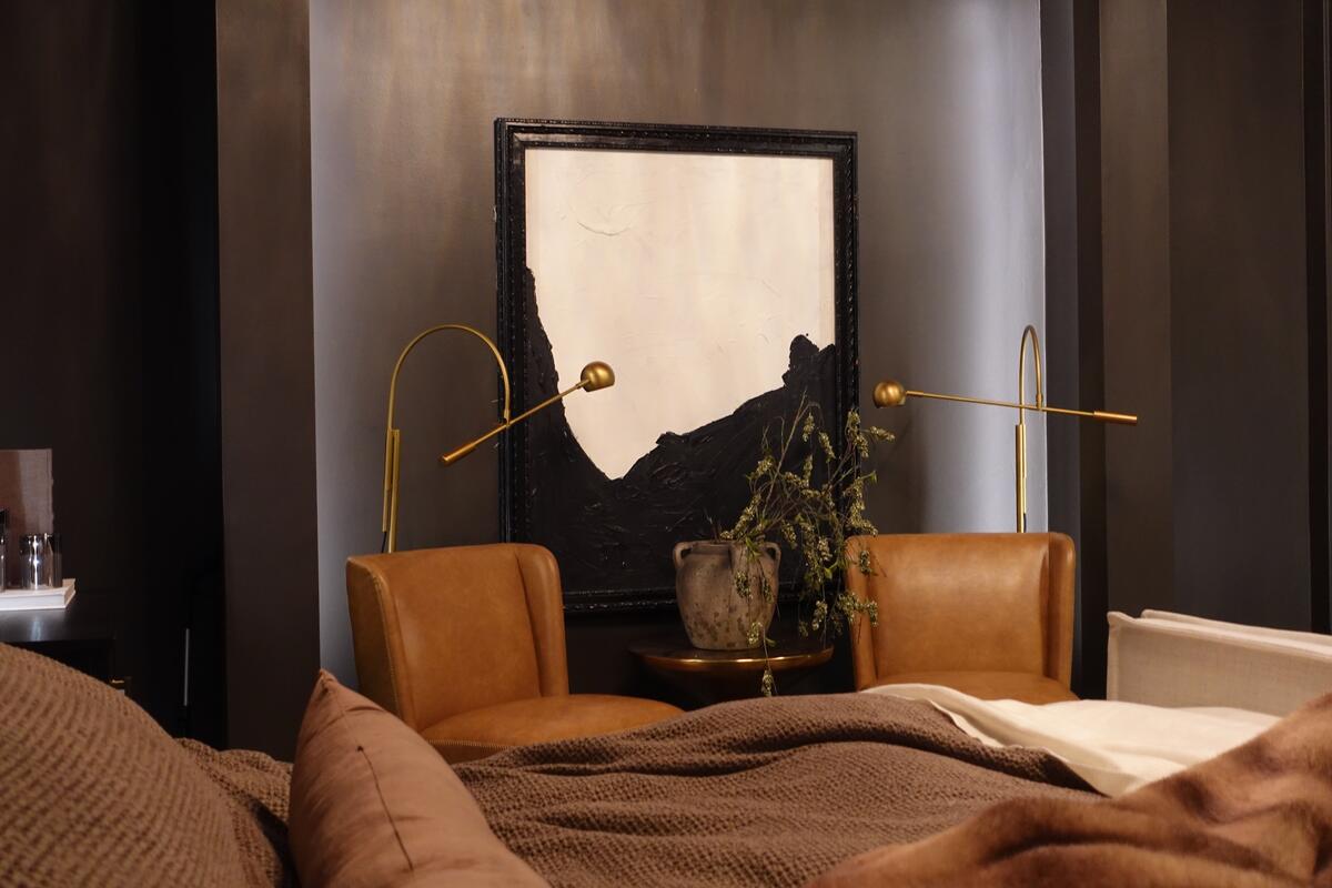 Brown leather chairs and brass lighting make up the sitting area in this moody bedroom