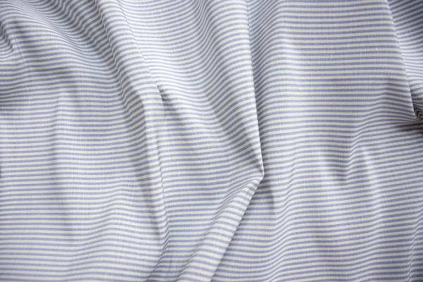 Sloane Stripe in Porcelain Blue: Our Sloane Stripe drapery is for those who crave a little pomp and circumstance. Updated in four ethereal colors, this traditional ticking stripe stands apart because of its silk-and-linen blend. Unlike most cottons, the linen creates a subtle slub across the weft, while the silk gives it an unmistakably lustrous finish. A juxtaposition of strength and elegance, this timeless drapery epitomizes luxury, and it effortlessly coordinates with the full Sloane collection.