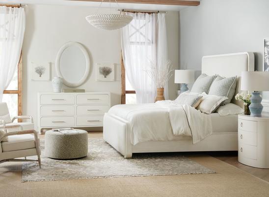 The casual, contemporary Ashore upholstered panel bed is finished in a painted white grasscloth and features soft edges that are echoed in the construction of the corresponding bedroom case pieces. The Wavecrest oval nightstand, finished in Shell, a soft, textured sandblasted white, has a beautifully honed marble veneer top. The accompanying six-drawer dresser is adorned with custom bar pulls in a light champagne finish.