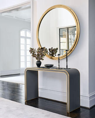 Modern luxury: Above the curved Davies console in brass-trimmed vegan leather hangs the Round mirror from the new five-piece Chesapeake collection. Hand-made in brushed brass, the design incorporates simple rivets for a subtle industrial edge that evokes the portholes of a ship.
