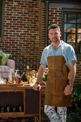 Actor Aiden Turner in a Moore & Giles apron with a bar cart featuring J. Earl & Sons vintage barware