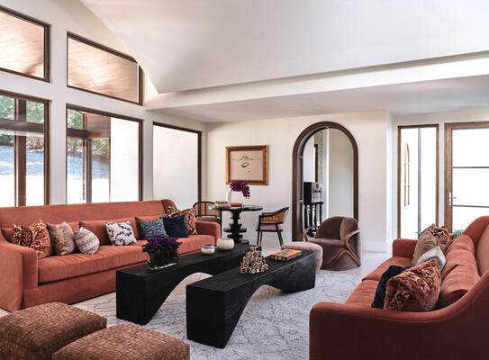 This large, open family room was designed with warmth and flexibility in mind. A pair of custom sofas feature a depth that invites some serious snuggling, with an assortment of pillows bringing   eclectic appeal. Dual benches in between accommodate all sorts of get-togethers, while a table at the back provides a perfect spot for jigsaw puzzles and card games.  
