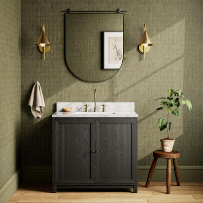 The Millie single wide vanity is crafted with a thick oak veneer base, Carrara marble top and iron hardware; on either side, French industrial–inspired Janna sconces feature the light antique brass finish of a vintage lamp 