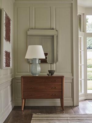 Framed by the Selborne mirror, the Hannington table lamp’s cool celadon base contrasts with the warm wood of the Colemore chest