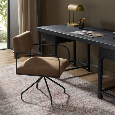 In the Fenn desk chair, a slim frame of black hammered iron supports cushioned seating upholstered in easy-to-clean Crypton performance fabric